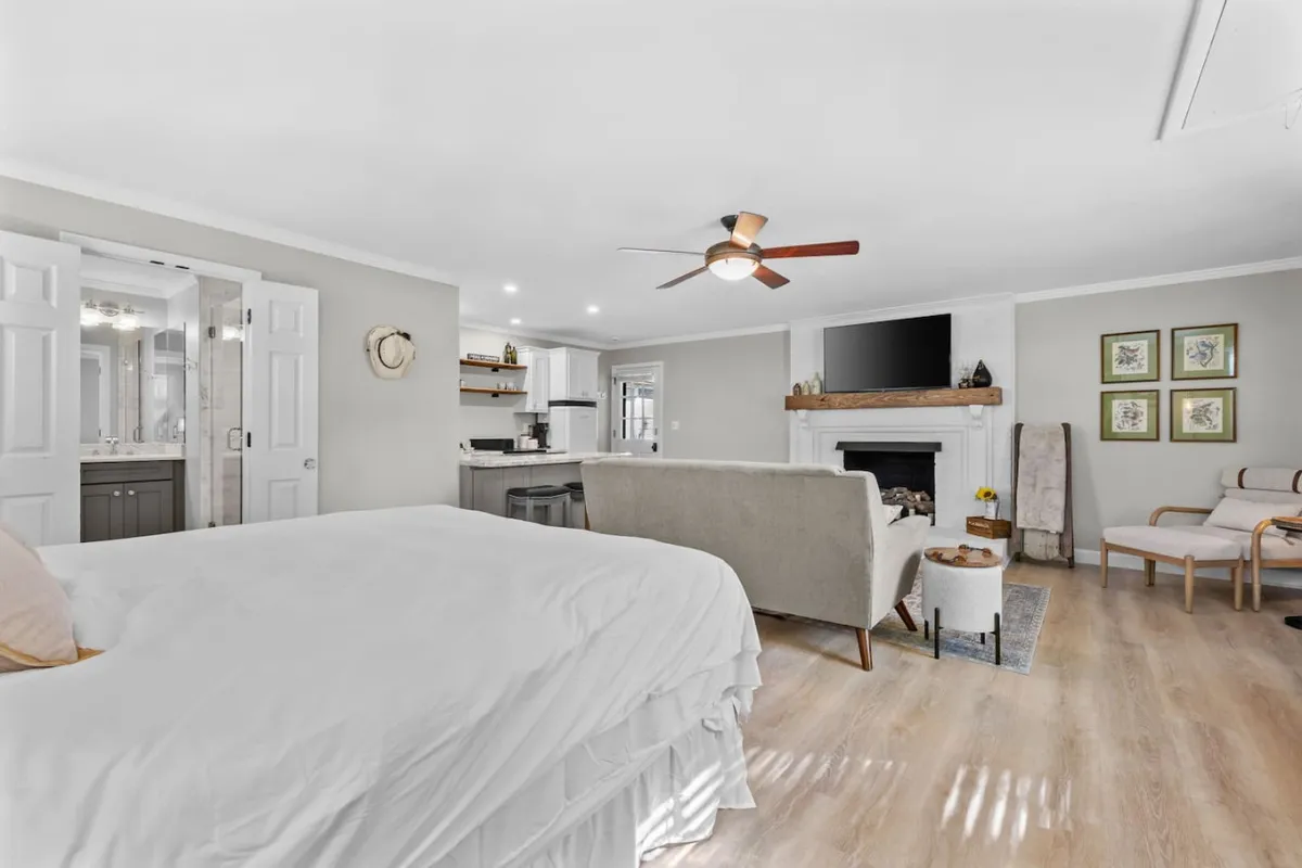 A serene bedroom with a comfortable bed, elegant fireplace, a cozy seating area, and decorative artwork. The space is designed for relaxation and togetherness, with soft natural light adding to the romantic feel.