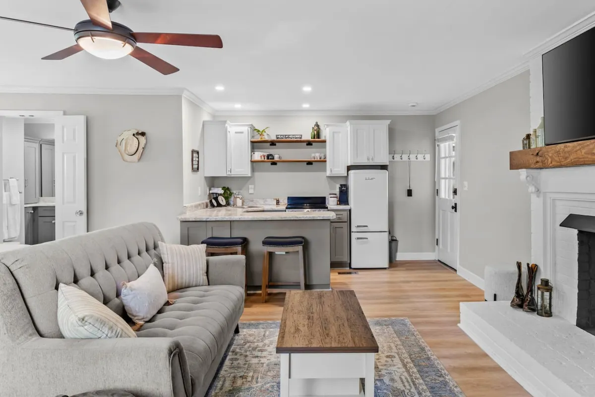 A welcoming living area centered around a comfy sofa and coffee table, with a kitchen island visible in the background and a fireplace anchoring the space. The arrangement suggests a cozy environment perfect for unwinding after a day of exploration, reading, or quiet reflection.