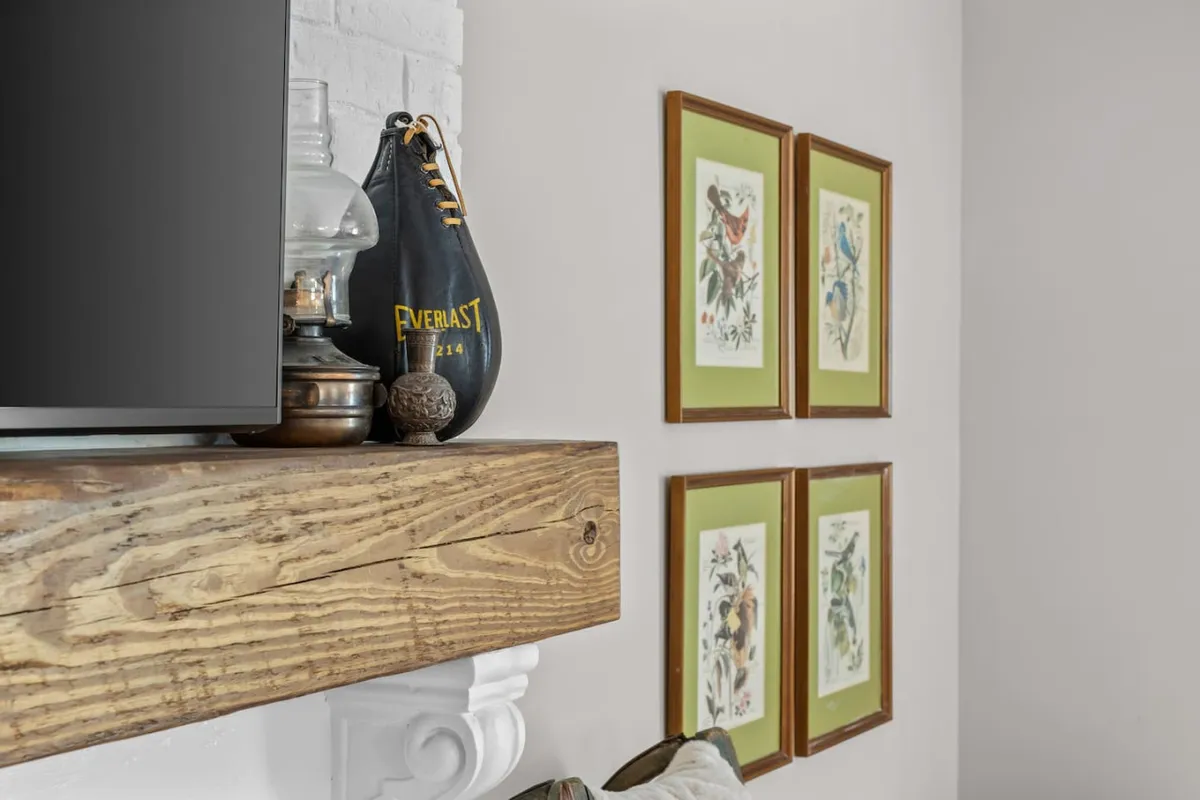A comfortable, personal living space featuring an ornate mantel, television, and framed artwork. Decorative objects add charm and character, hinting at the thoughtful touches throughout the cottage.