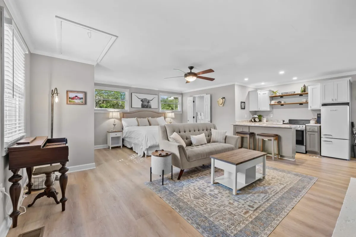 A multi-functional interior space showing a sofa, coffee table, bed, and a kitchen area. The area is open but thoughtfully arranged, indicating a comfortable space for relaxation, dining, and socializing as desired.