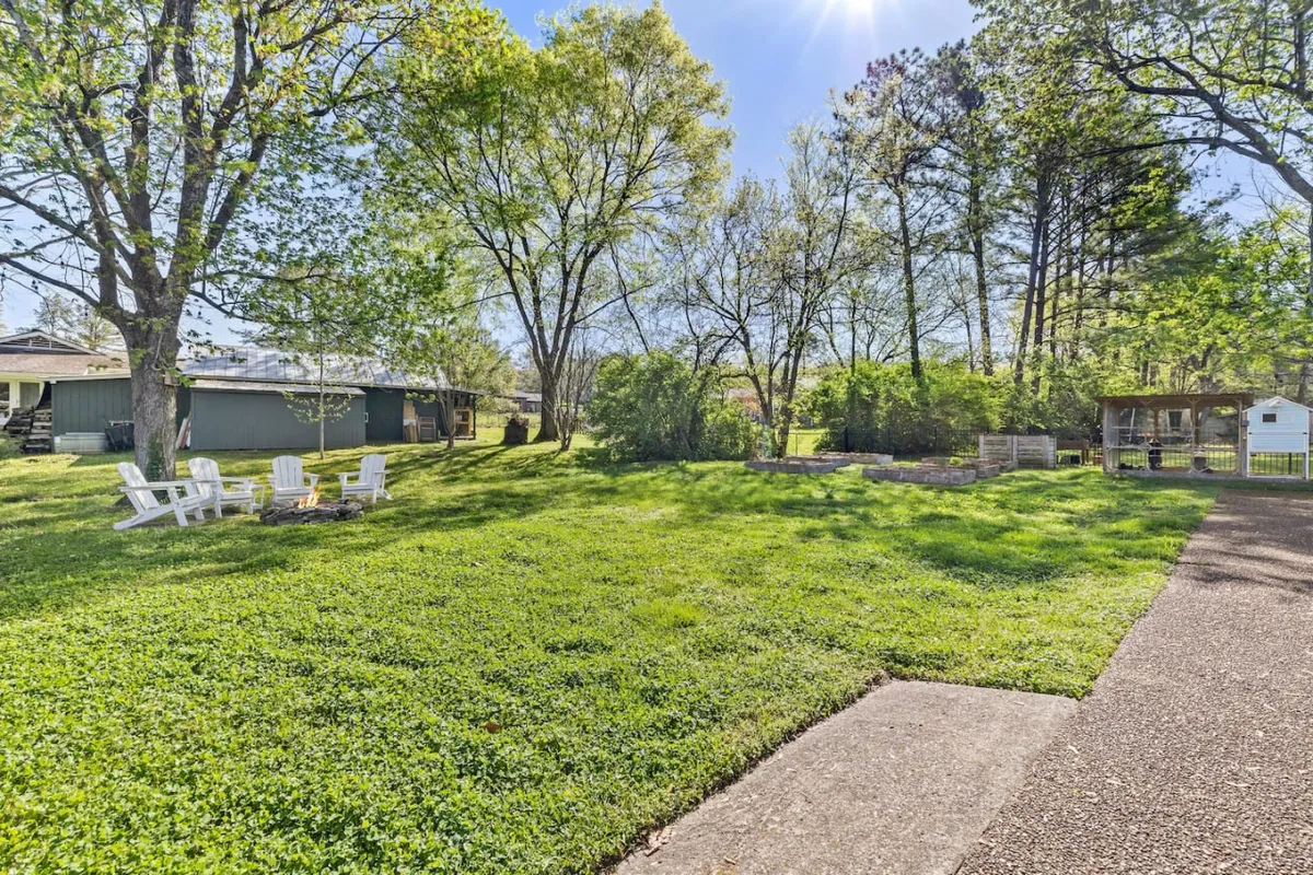 An inviting fire pit area set on green grass, surrounded by mature trees and comfortable outdoor seating. The scene suggests a welcoming spot for social gatherings, stargazing, and enjoying evenings together in nature.