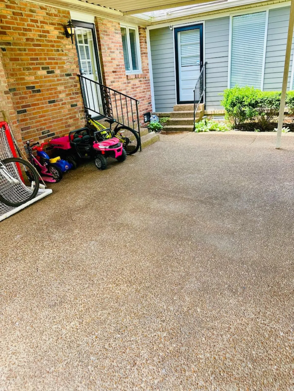 This exterior image highlights a family-friendly play area with colorful toys and bikes scattered near a brick wall and stairs leading to the main door. The casual, playful vibe suggests a space where children can play safely and freely.